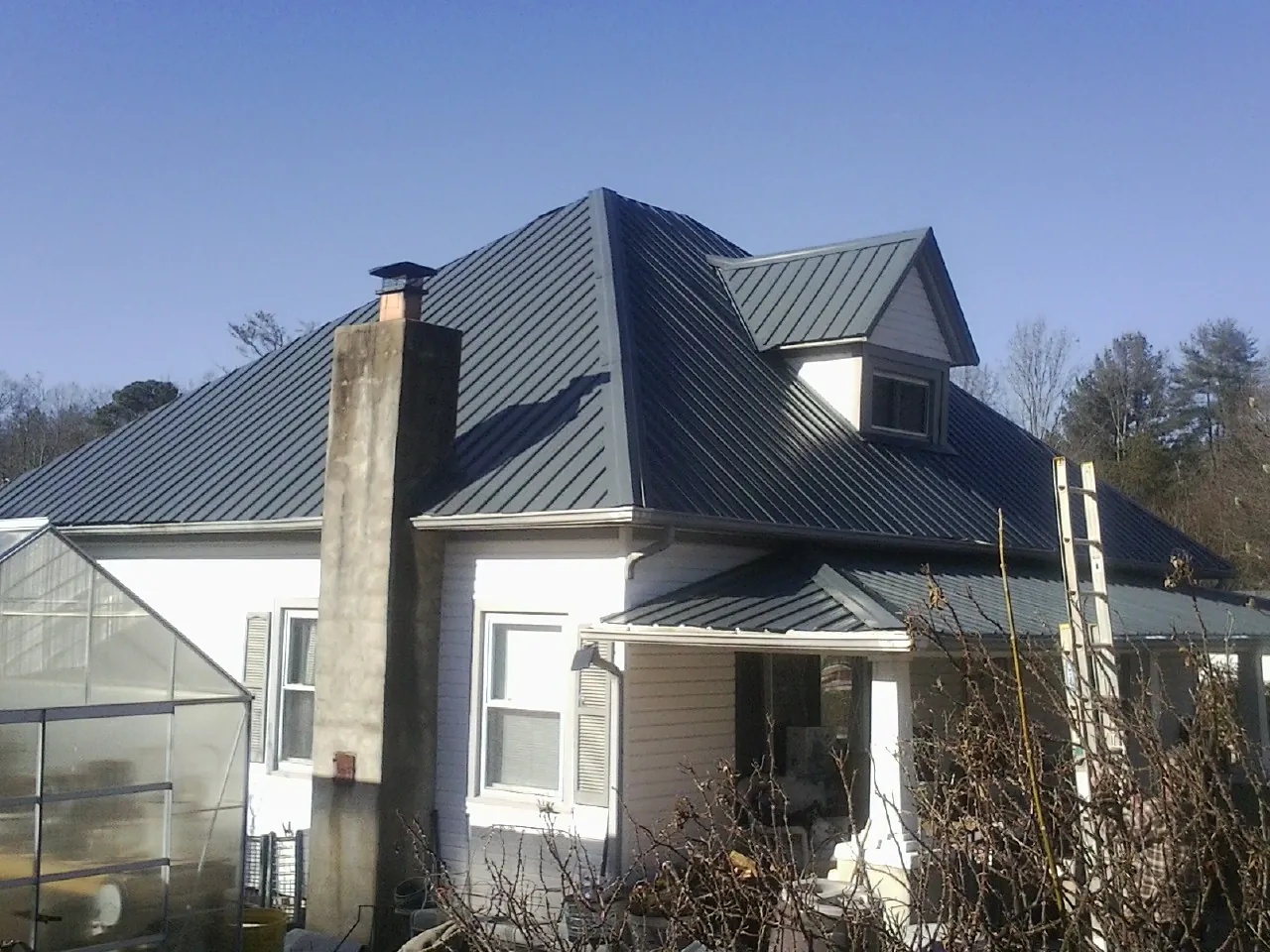 Dark blue standing seam metal roof on a white farmhouse with dormer — Slate & Tile Roof Repair by Roofing Brothers in Joy