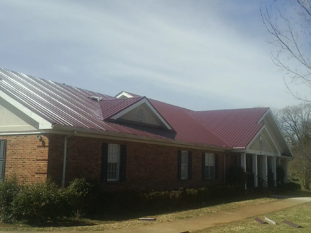 Red metal roof with gabled entries on a long brick building, from a Hail Damage Roof Repair job in Joy