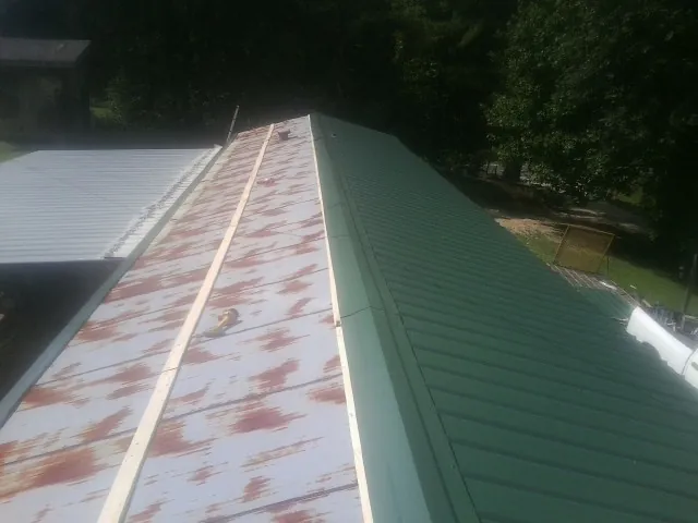 Old rusted panels beside newly installed green metal roofing — Wind Damage Roof Repair by Roofing Brothers in Joy