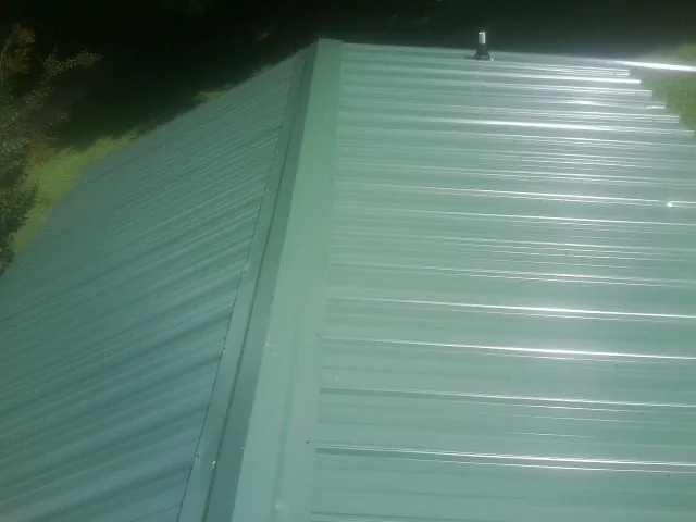 New green metal panels meeting at the ridge of a roof — Flat Roof Repair work by our crew in Joy