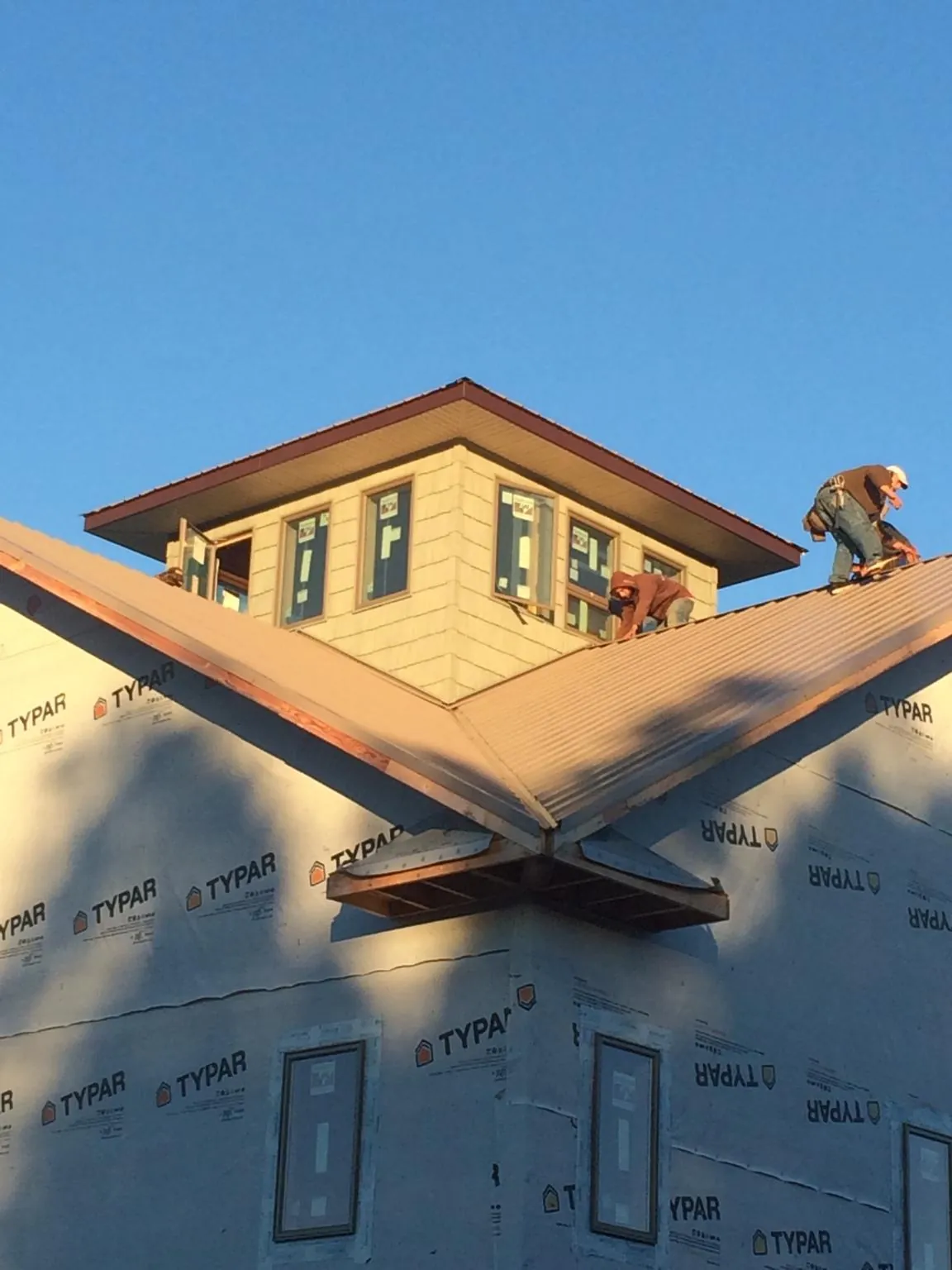 Roofers working around a rooftop cupola on a new metal roof at sunset — Roof Waterproofing in Joy by Roofing Brothers